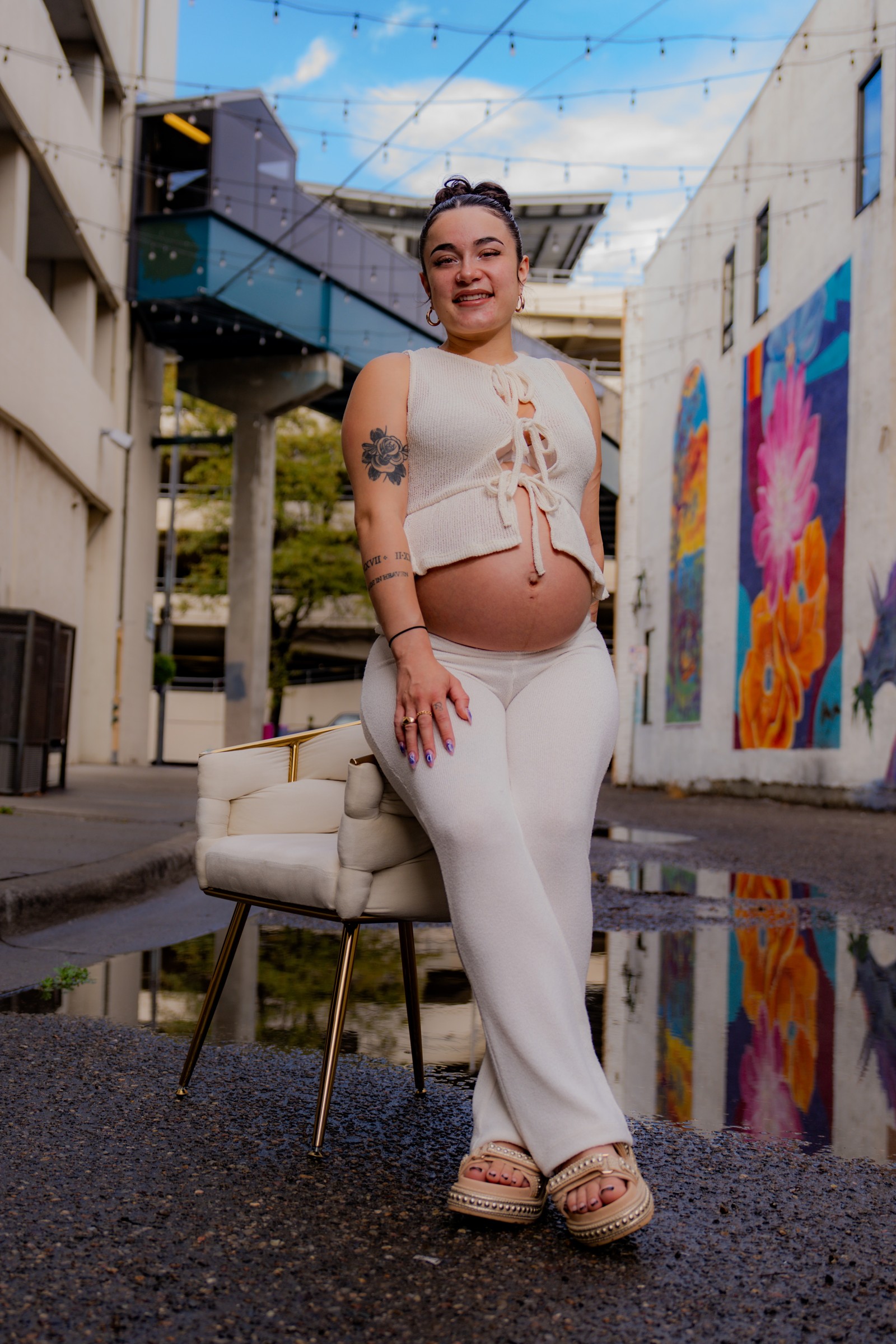 Expectant woman in a white outfit standing in a colorful urban alley
