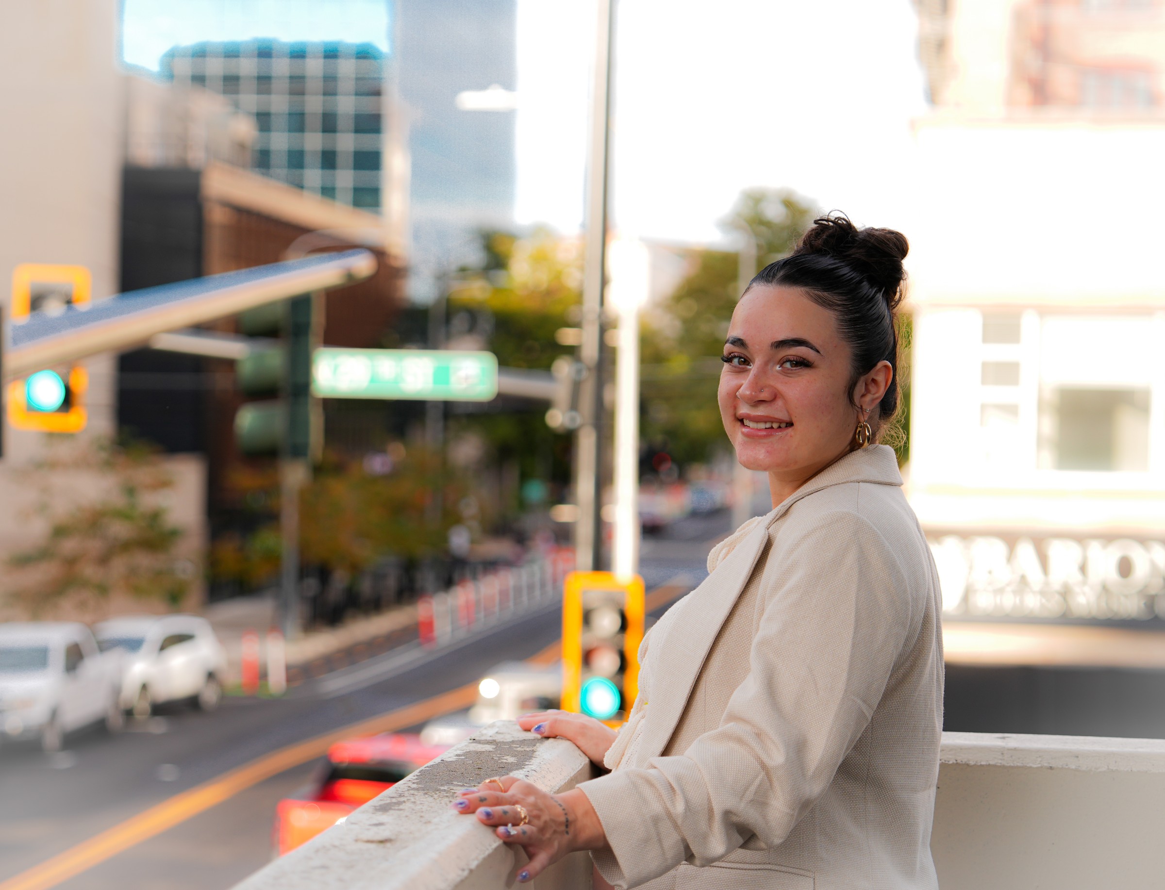 Smiling woman in a white jacket looking back from an urban balcony