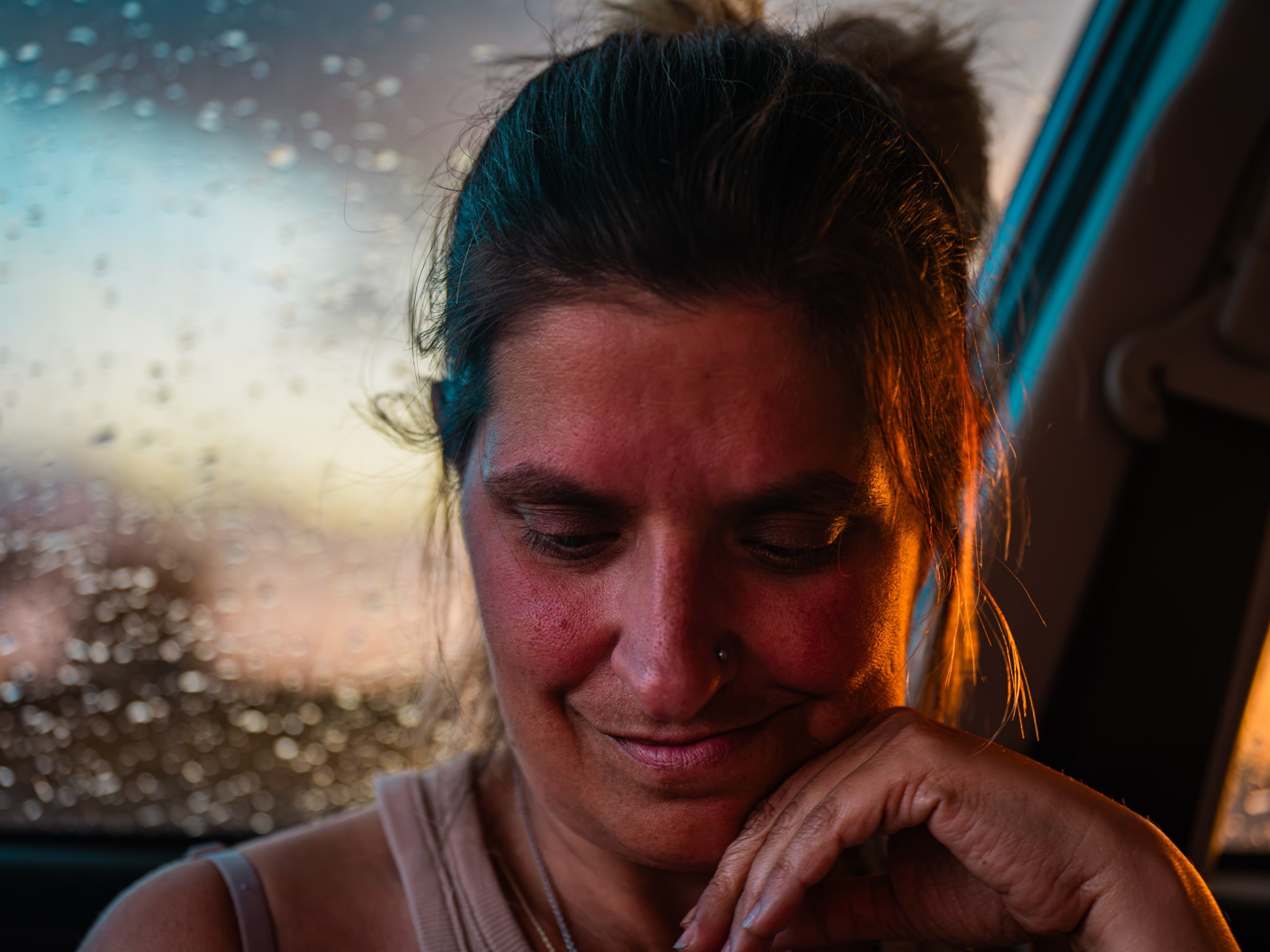 Close portrait of a woman beside a rain-speckled window in warm light