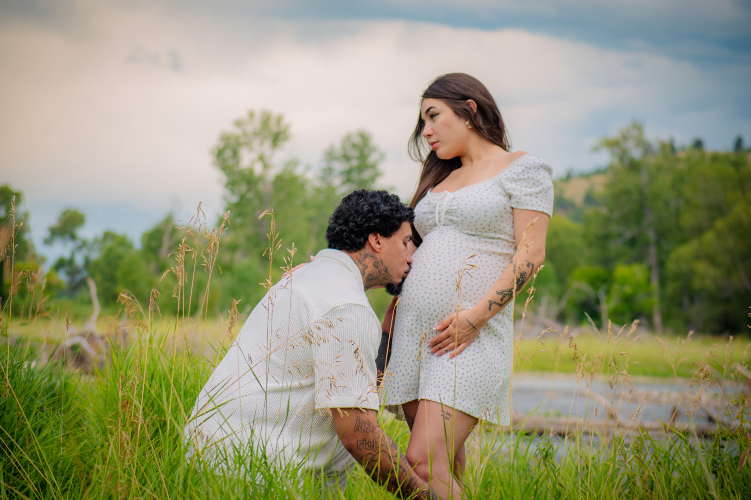 Expectant couple sharing a tender moment outdoors beside tall grass