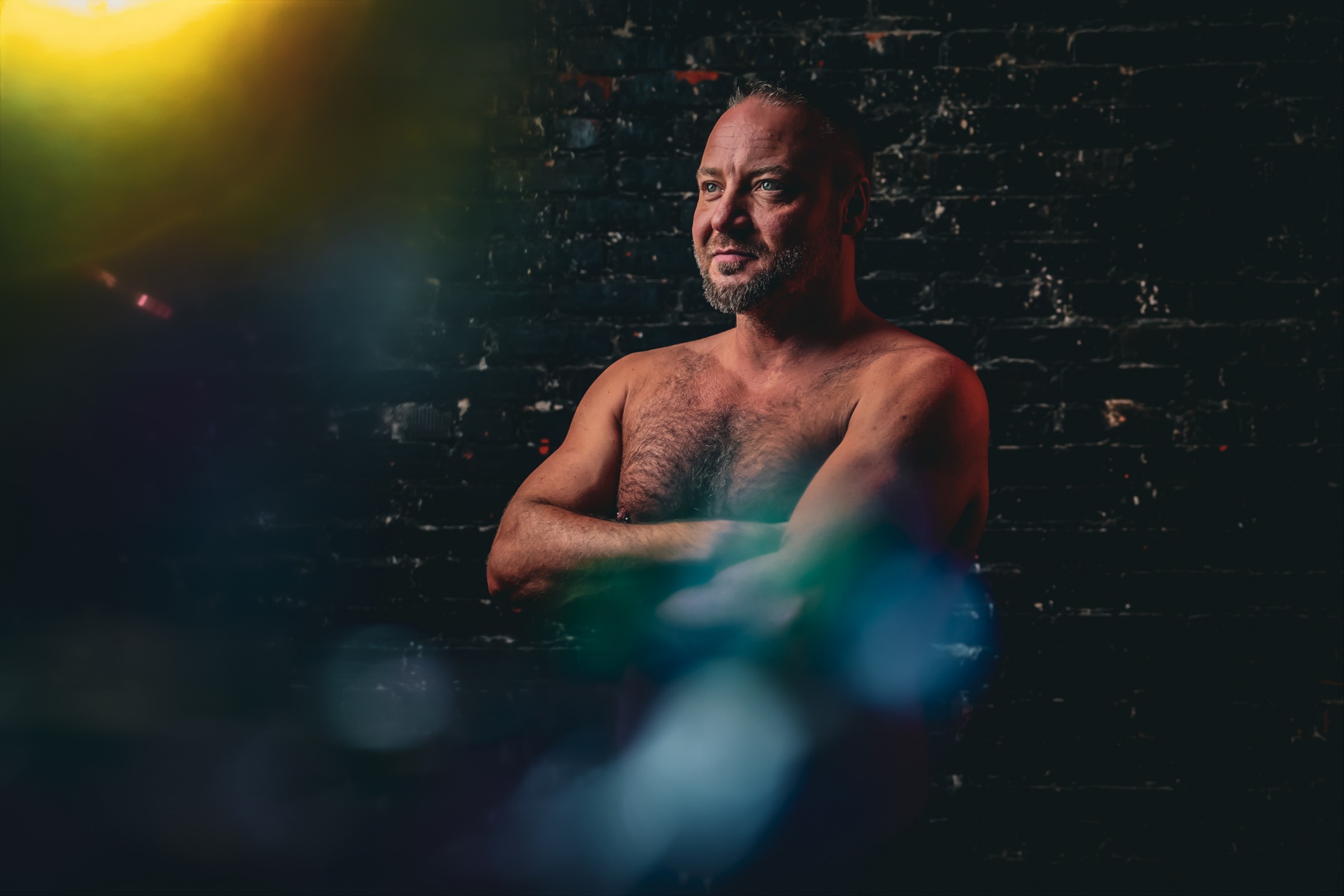 Man with folded arms against a dark textured wall in colored light