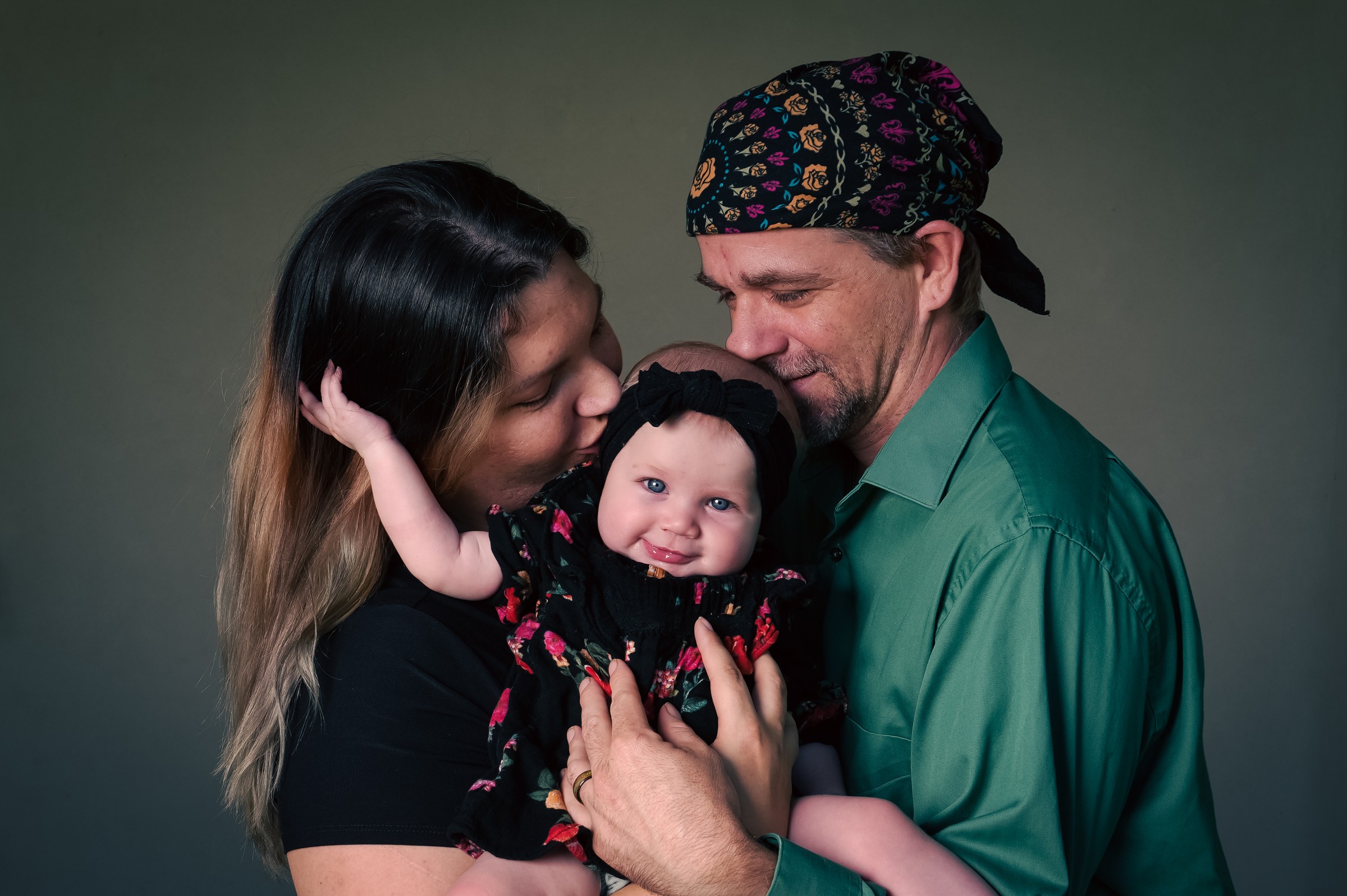Two parents holding their baby close against a dark background